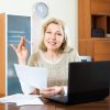 smiling-mature-woman-staring-financial-documents-table-home-interior-40153140